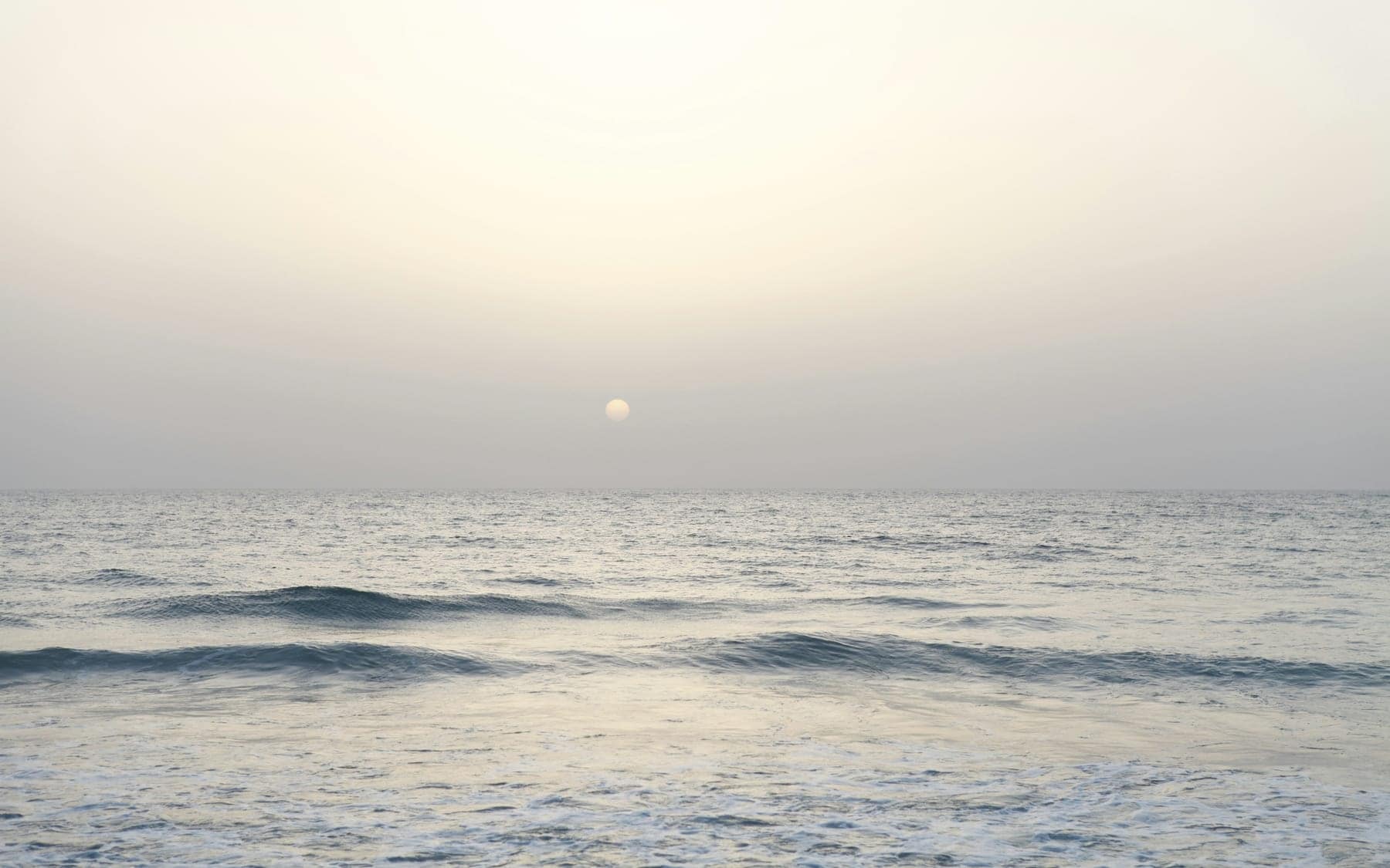 Mar calmo sob o sol baixo da manhã, com o horizonte dissolvido na bruma.